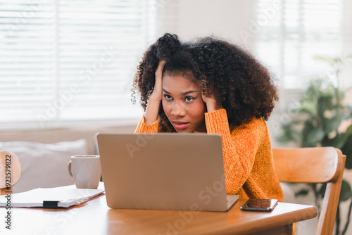 African American woman holding her forehead in frustration while working on a laptop, showcasing stress and exhaustion.