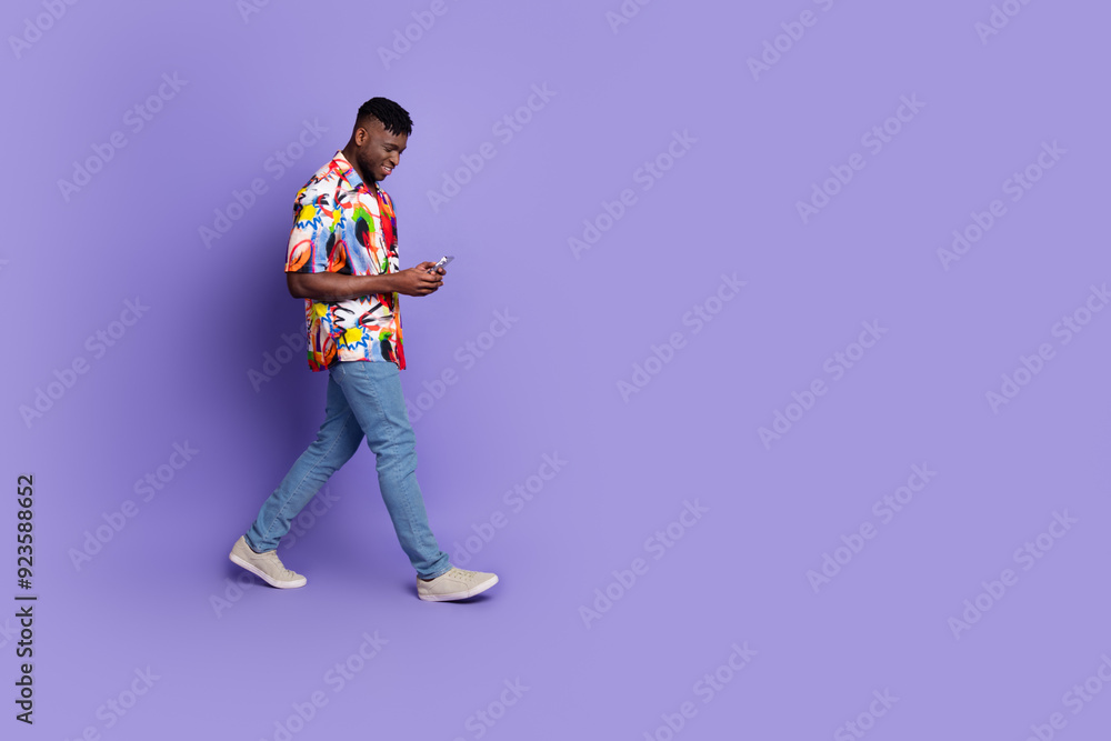Full length photo of handsome young guy hold device walking dressed stylish colorful garment isolated on purple color background Full length photo of handsome young guy hold device walking dressed stylish colorful garment isolated on purple color background