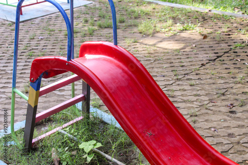 Selective focus of an abandoned playground in a city park containing a red slide, a scary or eerie or creepy atmosphere.