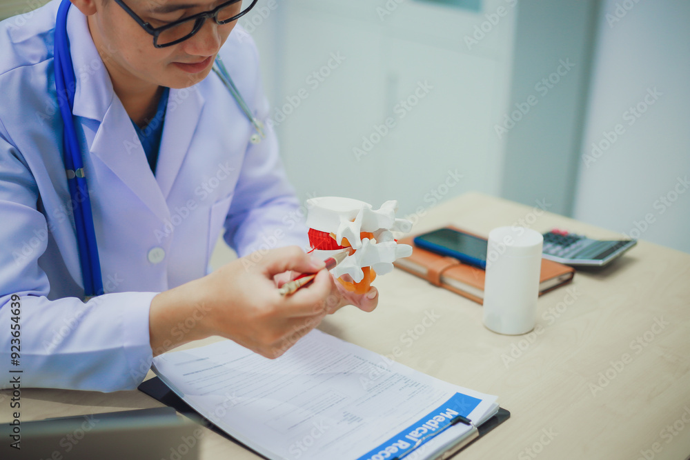 Orthopedist and surgeon using model or anatomical model of spine to educate patient about back pain on white background in examination room. Spinal stenosis or back pain. Medical. Orthopedist and surgeon using model or anatomical model of spine to educate patient about back pain on white background in examination room. Spinal stenosis or back pain. Medical.