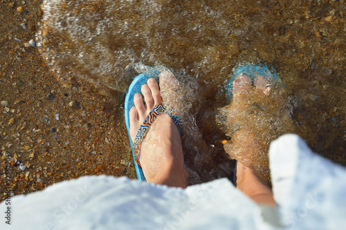 women's feet in shales on the sandy seashore. summer vacation. water, background for decoration