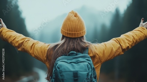 An adventurer clad in a mustard yellow jacket and a matching beanie raises their arms triumphantly on a mountain path, symbolizing freedom and exploring the boundless outdoors and nature. photo