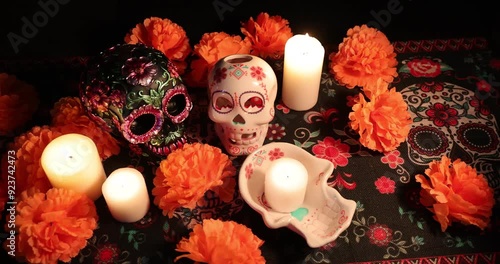 Two skulls, one glowing with an internal candle and the other decorated with metallic flowers, sit among marigolds. The peaceful placement of candles brings to life the spirit of Día de los Muertos. photo