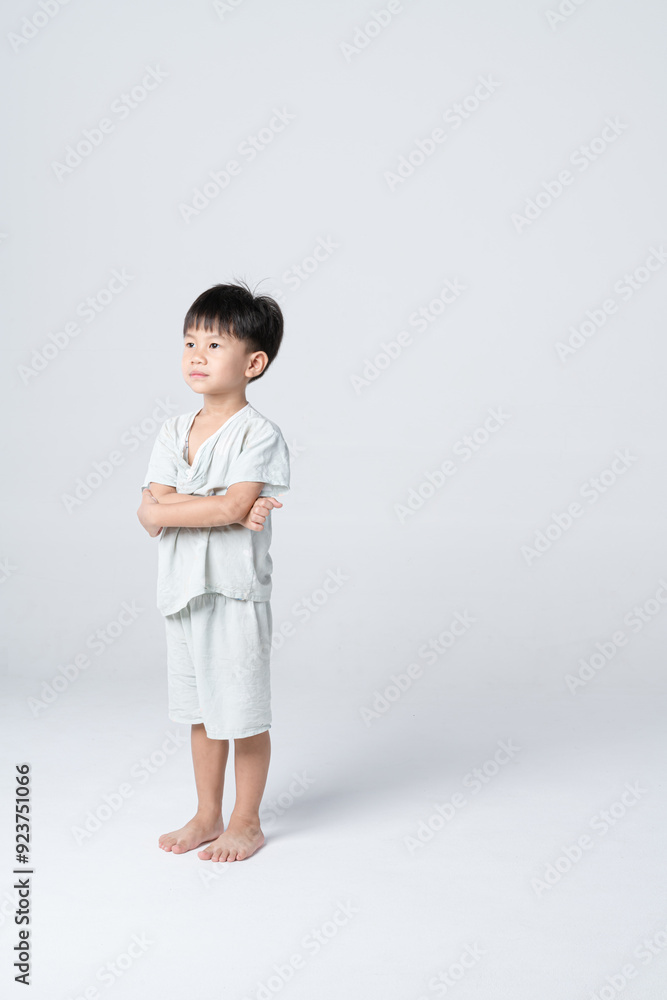 Asian child standing barefoot with arms crossed, looking serious or contemplative in a studio setting. Asian child standing barefoot with arms crossed, looking serious or contemplative in a studio setting.