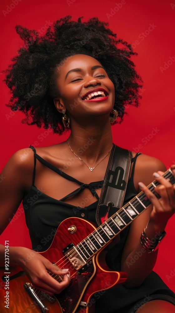 Obraz premium A joyful woman is playing her electric guitar, smiling against a bright red backdrop