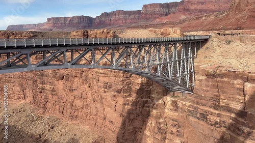 A California Condor soars gracefully beneath the Navajo Bridge, showcasing the breathtaking beauty of Marble Canyon in Arizona. A stunning backdrop of towering red rock cliffs and the arched bridge.  photo