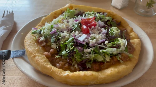 Close-up shot of a Navajo Taco, a traditional Native American frybread topped with beans, lettuce, tomatoes, cheese, and onions, served in an Arizona restaurant. Fresh and tasty ingredients - USA 