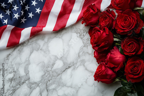 A striking top-down view of a patriotic floral tribute, featuring a vibrant American flag gracefully draped over a marble surface, adorned with a cluster of deep red roses. photo