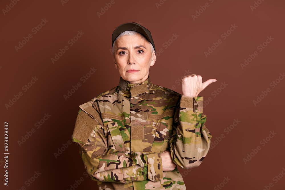 Photo of pretty senior female courageous servicewoman point empty space wear camouflage military uniform isolated on brown color background Photo of pretty senior female courageous servicewoman point empty space wear camouflage military uniform isolated on brown color background