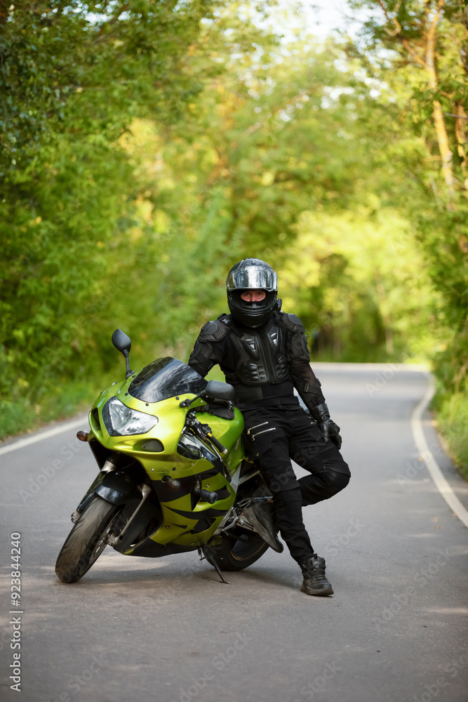 Obraz premium motorcyclist in black protective suit and helmet near green sports motorcycle