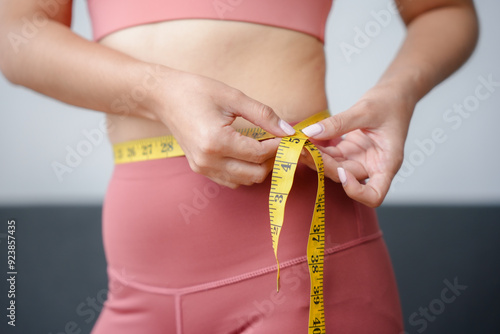 Tablou pe pânză Woman is measuring her waist with a yellow measuring tape, checking the progress