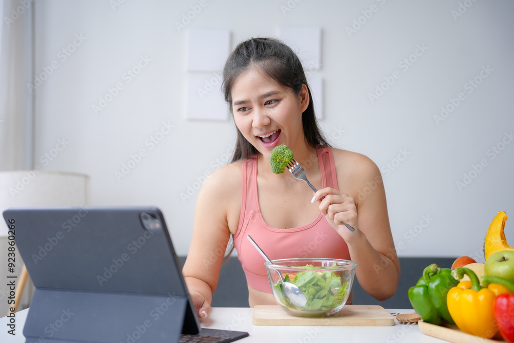Young woman is enjoying a healthy meal of salad while having a video call on her tablet, promoting a balanced lifestyle Young woman is enjoying a healthy meal of salad while having a video call on her tablet, promoting a balanced lifestyle