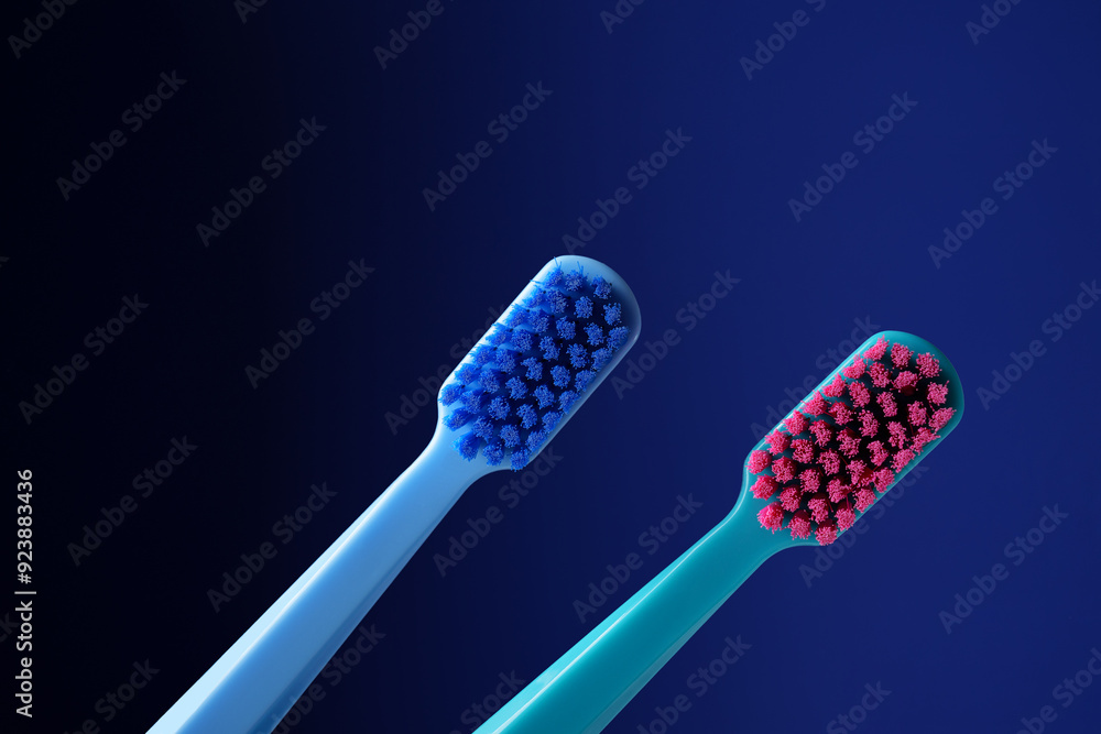 Horizontal photo. Two bright plastic toothbrushes on a dark blue background. Horizontal photo. Two bright plastic toothbrushes on a dark blue background.