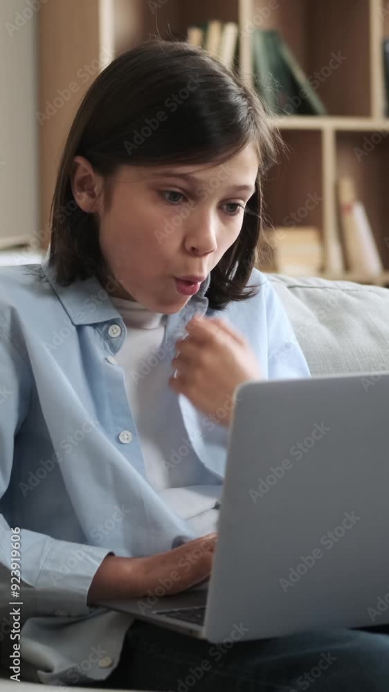Amazed and astonished Caucasian young boy receiving good news online and exclaiming wow using laptop, resting on sofa at home. Vertical video. Amazed and astonished Caucasian young boy receiving good news online and exclaiming wow using laptop, resting on sofa at home. Vertical video.