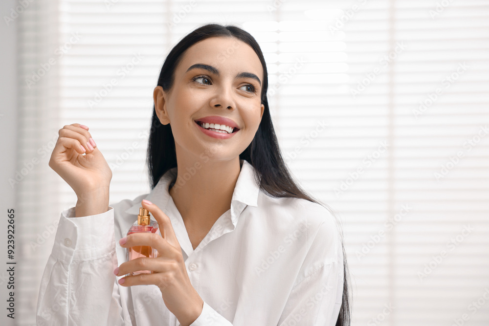 Smiling woman spraying aromatic perfume onto wrist at home. Space for text Smiling woman spraying aromatic perfume onto wrist at home. Space for text