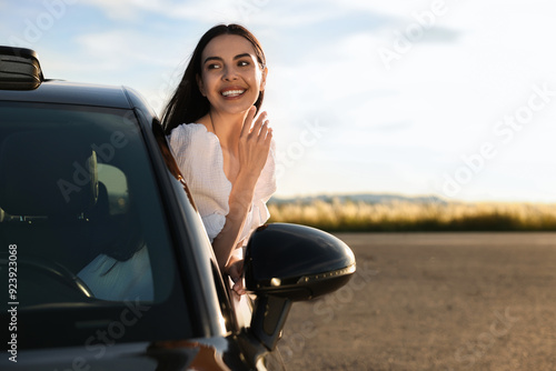 Smiling young woman leaning out of car window outdoors. Enjoying trip