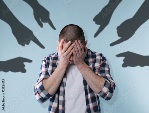 Silhouettes of people's hands pointing at upset man on light blue background. Social pressure, failure, responsibility