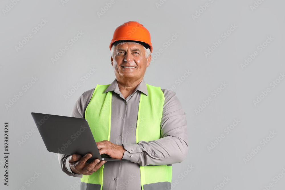 Engineer in hard hat with laptop on grey background, space for text Engineer in hard hat with laptop on grey background, space for text
