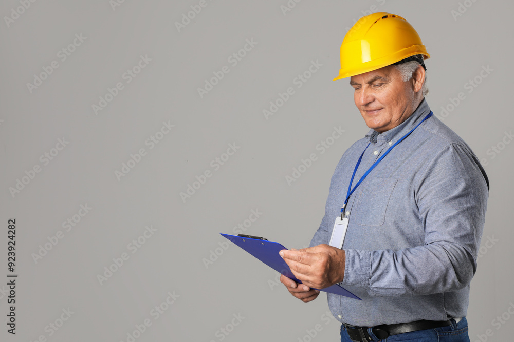 Engineer in hard hat with clipboard on grey background, space for text Engineer in hard hat with clipboard on grey background, space for text