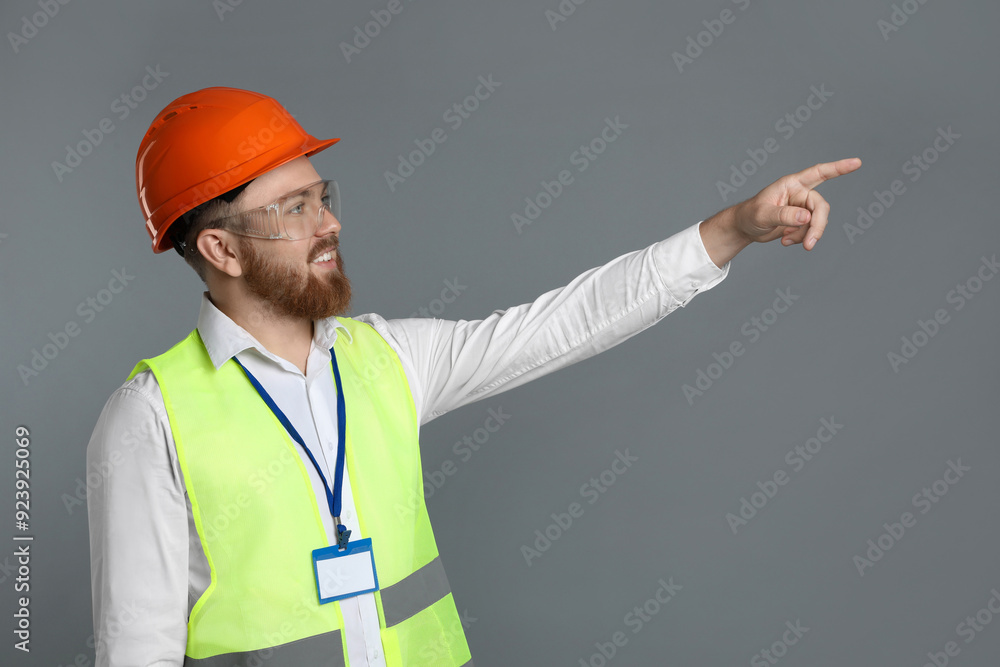 Engineer in hard hat and goggles pointing at something on grey background Engineer in hard hat and goggles pointing at something on grey background