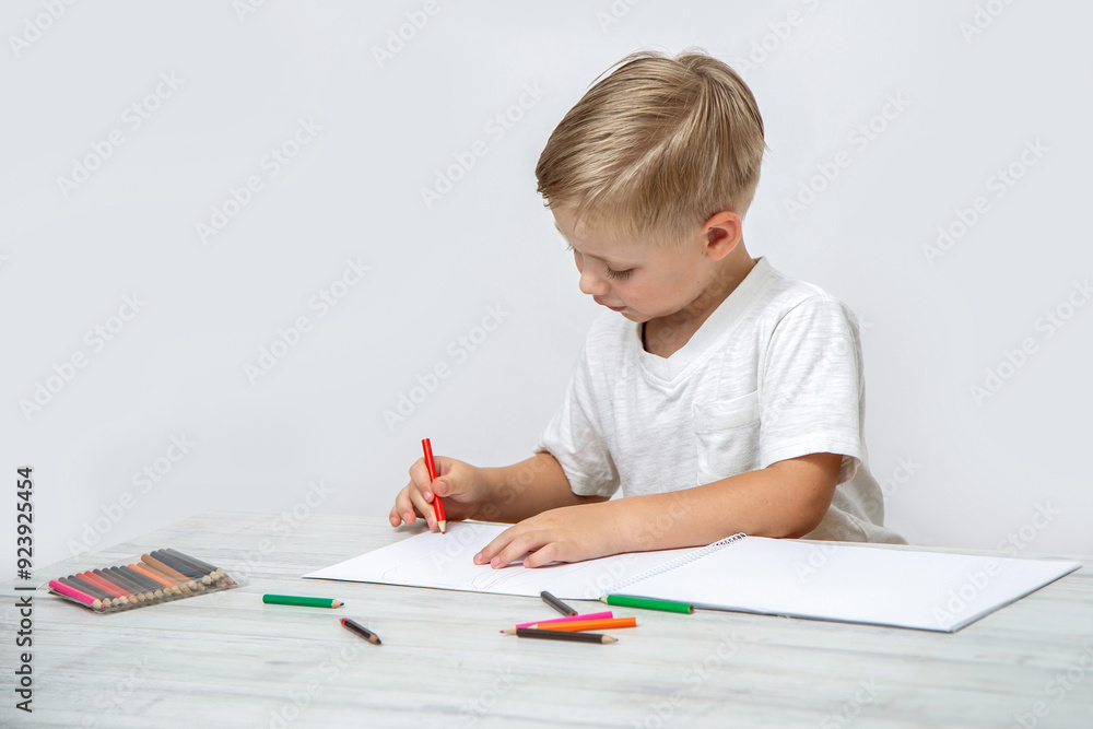 A toddler draws with colored pencils in a sketchbook while sitting at a table in the nursery. A toddler draws with colored pencils in a sketchbook while sitting at a table in the nursery.