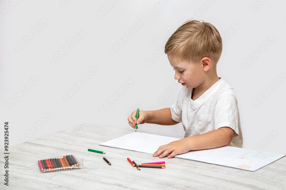 A toddler draws with colored pencils in a sketchbook while sitting at a table in the nursery. A toddler draws with colored pencils in a sketchbook while sitting at a table in the nursery.