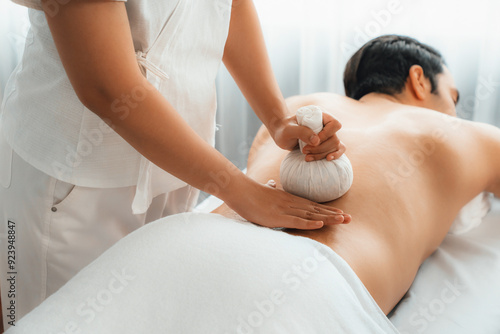 Hot herbal ball spa massage body treatment, masseur gently compresses herb bag on man body. Tranquil and serenity of aromatherapy recreation in day lighting ambient at spa salon. Quiescent