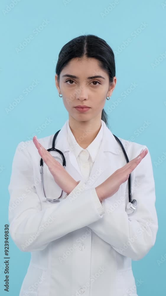 Stern Caucasian female doctor or nurse showing stop gesture with crossed arms on blue background. Concept of a protection. Vertical video.