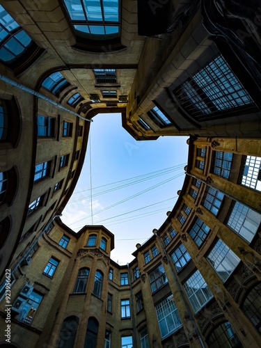 A dramatic upward view of a historic courtyard with curved architecture, emphasizing the symmetry and intricate details of the building against a clear blue sky. The image captures the unique