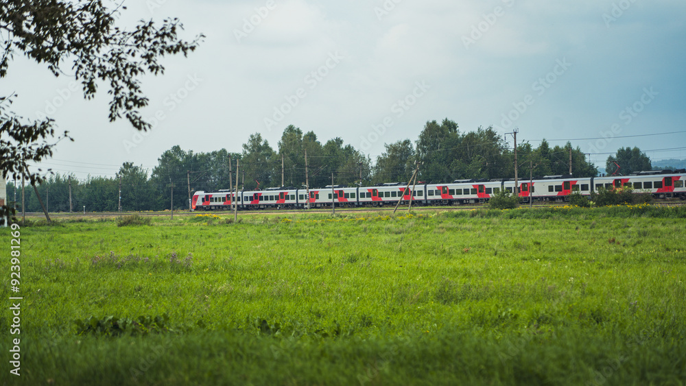 A high-speed electric train travels along a green field. A train in the distance A high-speed electric train travels along a green field. A train in the distance