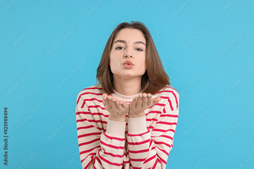 Beautiful teenage girl blowing kiss on light blue background Beautiful teenage girl blowing kiss on light blue background