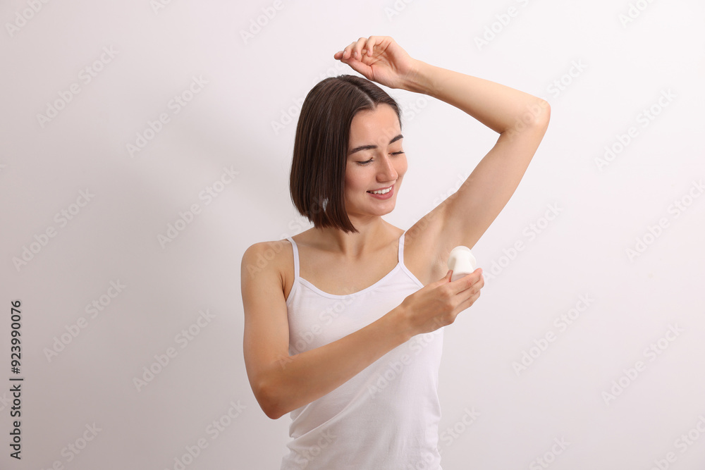 Smiling woman applying roll-on deodorant on white background
