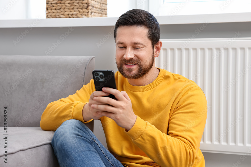 Happy man using smartphone near heating radiator at home Happy man using smartphone near heating radiator at home