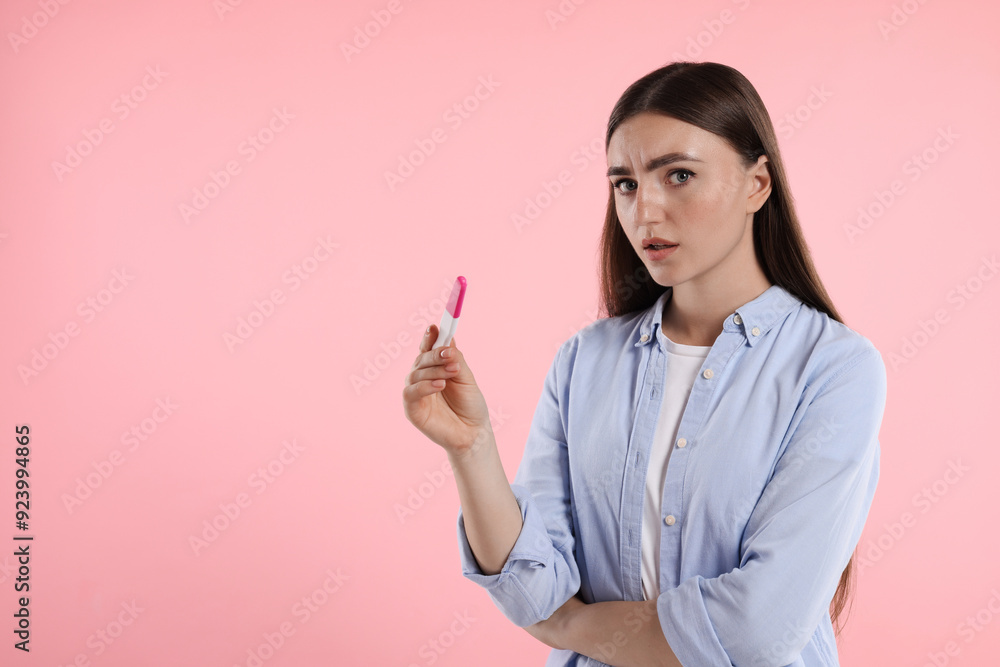 Confused woman holding pregnancy test on pink background, space for text Confused woman holding pregnancy test on pink background, space for text