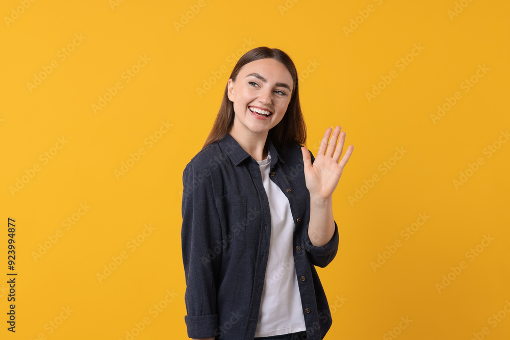 Happy young woman waving on orange background Happy young woman waving on orange background