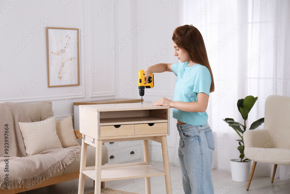 Woman with electric screwdriver assembling table in room Woman with electric screwdriver assembling table in room