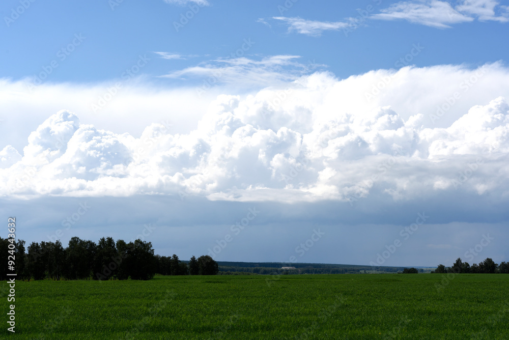 Thunderclouds on the background of a green field. A stormy landscape in the countryside. Thunderclouds on the background of a green field. A stormy landscape in the countryside.