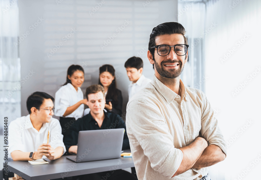 Confidence and happy smiling businessman portrait with background of his colleague and business team working in office. Office worker teamwork and positive workplace concept. Prudent Confidence and happy smiling businessman portrait with background of his colleague and business team working in office. Office worker teamwork and positive workplace concept. Prudent
