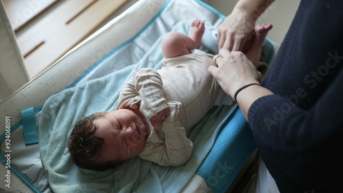 Mother adjusting newborn baby's outfit, lying on changing table, tenderly dressing infant, capturing intimate moments of care and love, highlighting parental bonding, early parenthood