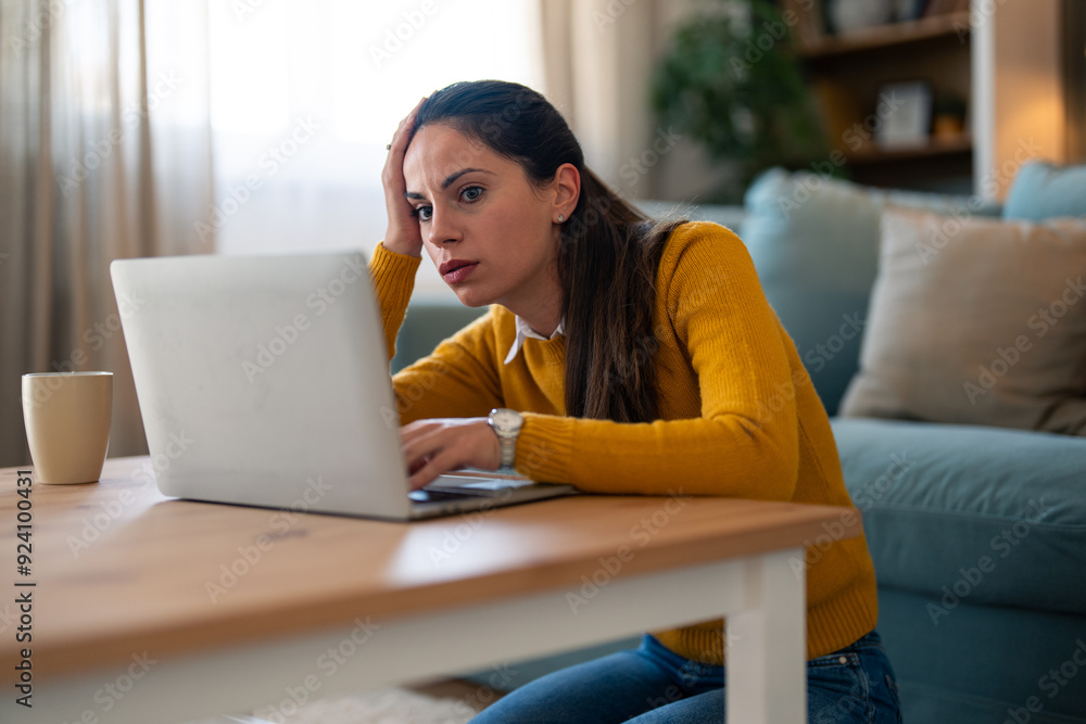 A stressed Caucasian woman in casual attire is focused on her laptop, seated on the floor by a coffee table in a living room, signaling a challenging moment during remote work. A stressed Caucasian woman in casual attire is focused on her laptop, seated on the floor by a coffee table in a living room, signaling a challenging moment during remote work.