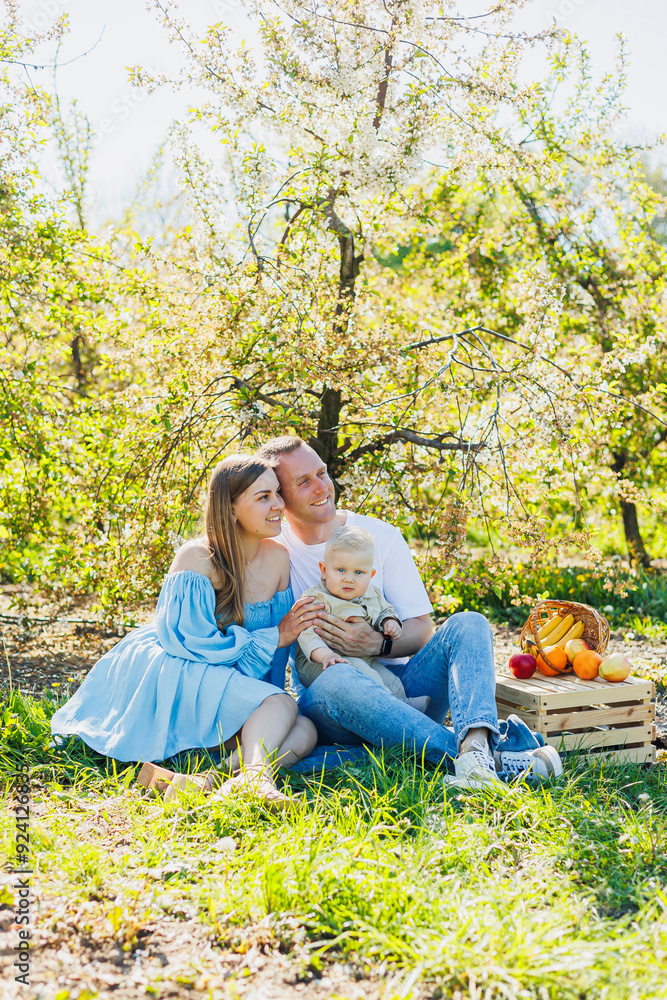 Fototapeta premium Father and mother holding little son in nature, concept of beautiful family bonds. Family portrait of parents with a little son. The concept of a happy family