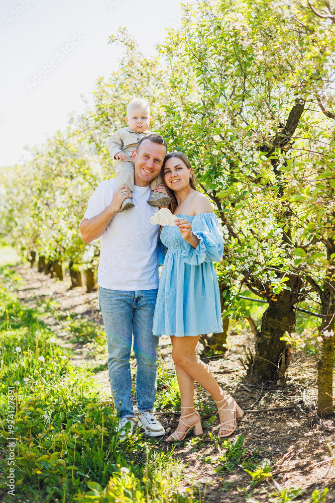 Fototapeta premium Father and mother holding little son in nature, concept of beautiful family bonds. Family portrait of parents with a little son. The concept of a happy family