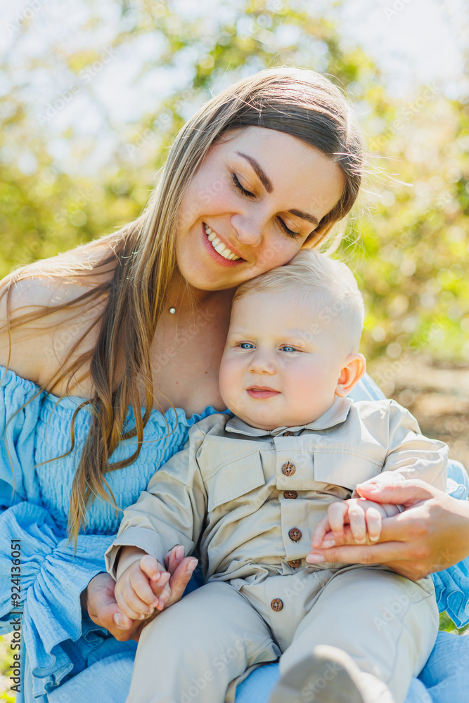 A young happy mother holds her little son in her arms while standing in nature. A walk with a child. Mother on maternity leave on a walk with a baby. A young happy mother holds her little son in her arms while standing in nature. A walk with a child. Mother on maternity leave on a walk with a baby.
