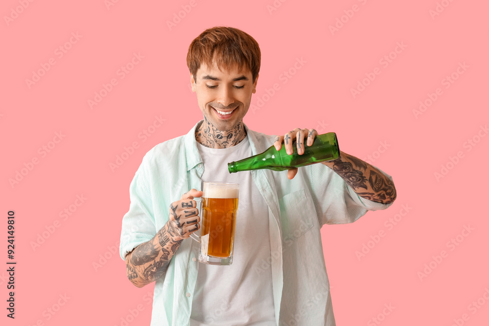 Tattooed young happy man pouring beer into glass on pink background Tattooed young happy man pouring beer into glass on pink background