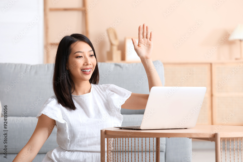 Beautiful young Asian woman with laptop waving hand at home Beautiful young Asian woman with laptop waving hand at home
