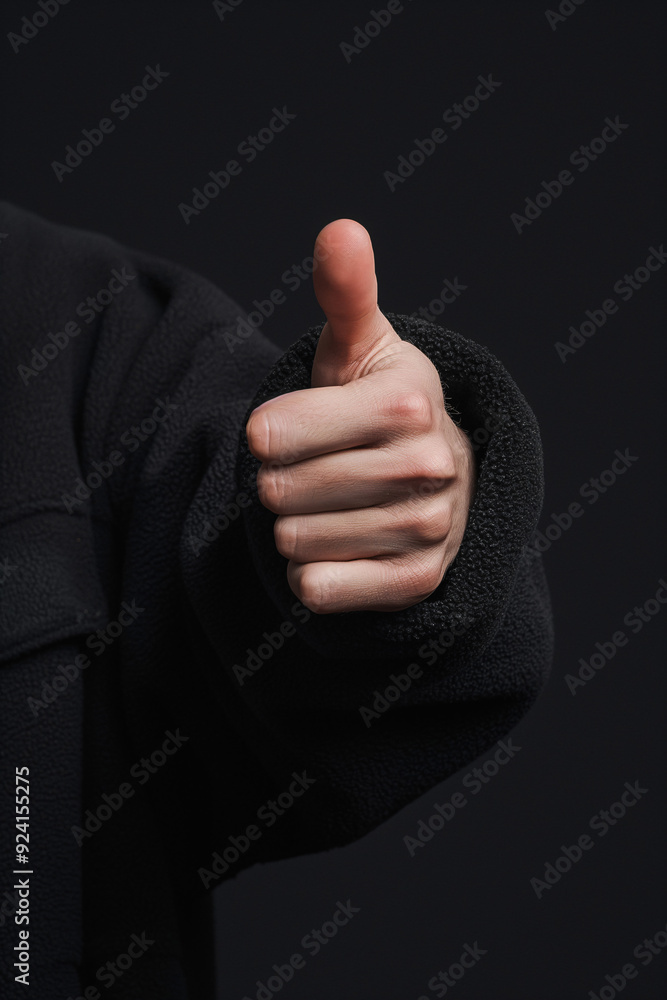 A hand shows a thumbs-up gesture, signaling approval or encouragement amidst a simple black backdrop A hand shows a thumbs-up gesture, signaling approval or encouragement amidst a simple black backdrop