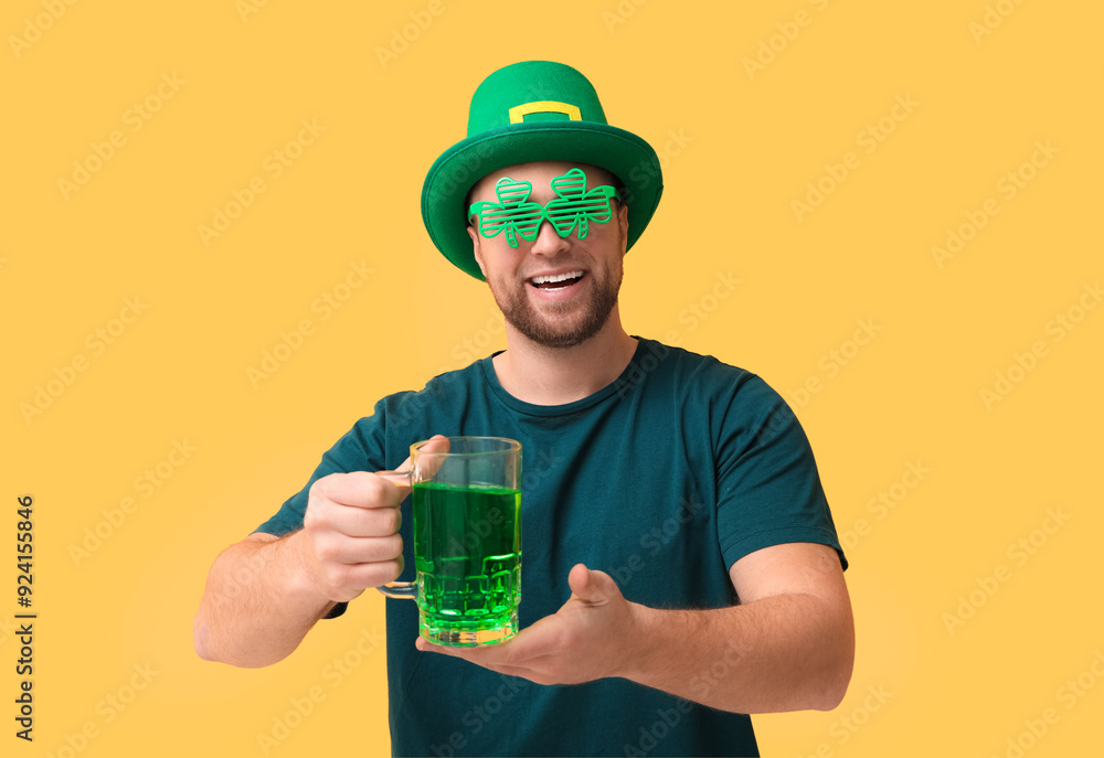 Happy young man in leprechaun's hat with mug of beer on yellow background. St. Patrick's Day celebration Happy young man in leprechaun's hat with mug of beer on yellow background. St. Patrick's Day celebration