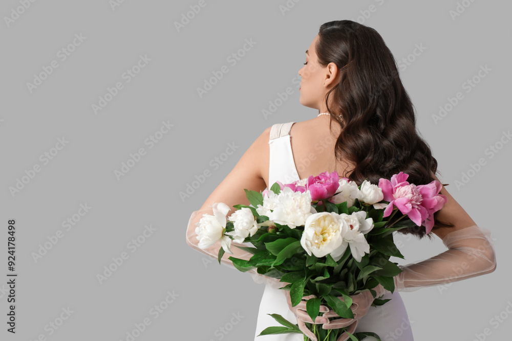 Young woman with bouquet of peony flowers on grey background, back view Young woman with bouquet of peony flowers on grey background, back view