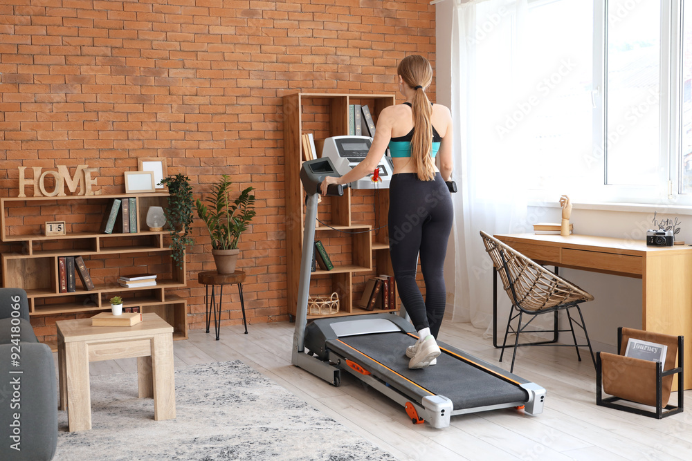 Fototapeta premium Sporty woman on treadmill training at home, back view