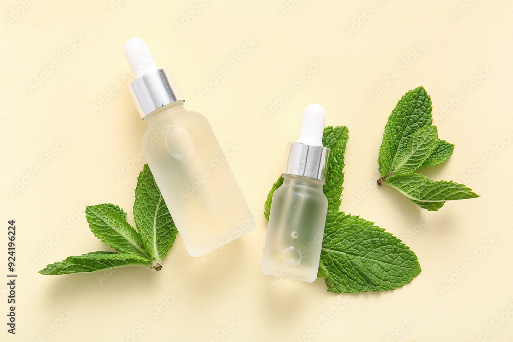 Bottles of essential oil and mint leaves on beige background Bottles of essential oil and mint leaves on beige background